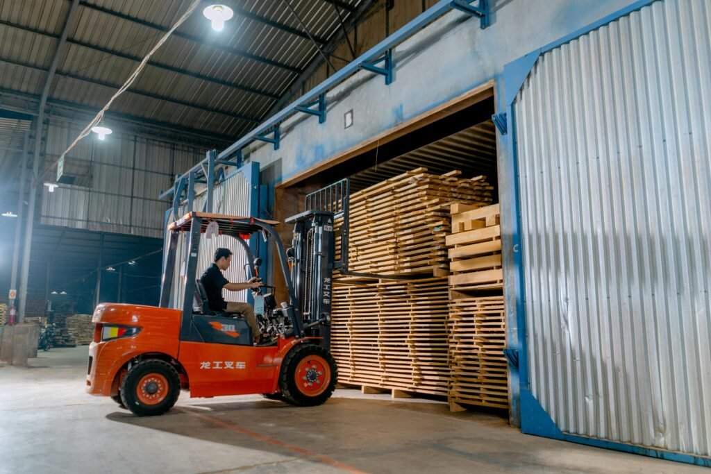 Man operating a forklift indoors loading wooden pallets in a warehouse.